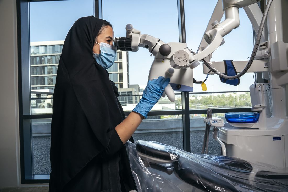 A clinician at Tam Dental working at a dental operating microscope beside a window in Jeddah.